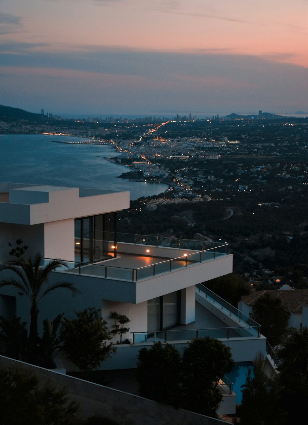 Modern villa overlooking a coastal city at night.